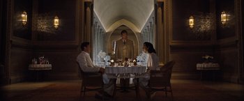 Movie still from “Death on the Nile” (2022), directed by Kenneth Branagh – Two people sitting at a table with a man standing in the middle of the room; Wide shot, High angle