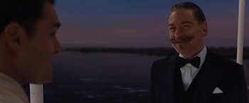 Movie still from “Death on the Nile” (2022), directed by Kenneth Branagh – A man in a black suit standing in front of a body of water; Close Up shot, Over the shoulder angle