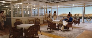 Movie still from “Death on the Nile” (2022), directed by Kenneth Branagh – A group of people sitting at a table in a room; Wide shot, Low angle