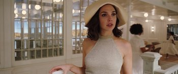 Movie still from “Death on the Nile” (2022), directed by Kenneth Branagh – A woman wearing a white hat standing in front of a window; Medium shot, Over the shoulder angle