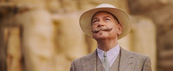 Movie still from “Death on the Nile” (2022), directed by Kenneth Branagh – An older man wearing a suit and hat smoking a cigarette; Close Up shot, Low angle