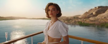 Movie still from “Death on the Nile” (2022), directed by Kenneth Branagh – A beautiful young lady wearing a white shirt and a white skirt; Medium shot, Low angle