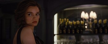 Movie still from “Death on the Nile” (2022), directed by Kenneth Branagh – A beautiful woman standing in front of a bunch of bottles; Close Up shot, Over the shoulder angle