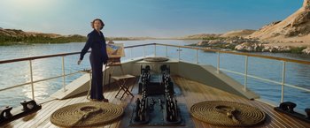 Movie still from “Death on the Nile” (2022), directed by Kenneth Branagh – A woman standing on top of a boat in front of a painting; Wide shot, High angle