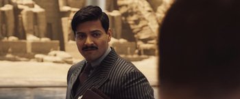 Movie still from “Death on the Nile” (2022), directed by Kenneth Branagh – A man in a suit and tie holding a book in his hand; Close Up shot, Over the shoulder angle