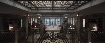 Movie still from “Death on the Nile” (2022), directed by Kenneth Branagh – Two people sitting on a bench inside a building; Wide shot, High angle