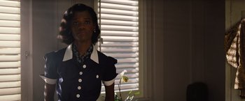 Movie still from “Death on the Nile” (2022), directed by Kenneth Branagh – A woman standing in front of a window with blinds; Medium shot, Low angle