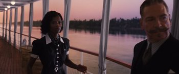 Movie still from “Death on the Nile” (2022), directed by Kenneth Branagh – A woman standing on a balcony overlooking a body of water; Medium shot, Over the shoulder angle