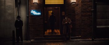 Movie still from “Death on the Nile” (2022), directed by Kenneth Branagh – A man standing in front of a building at night looking at his cell phone; Wide shot, Low angle