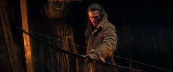 Movie still from “The Hobbit: The Battle of the Five Armies” (2014), directed by Peter Jackson – A man holding a bow and arrow while wearing a brown coat; Medium shot, Over the shoulder angle
