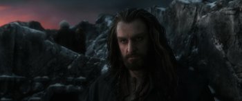 Movie still from “The Hobbit: The Battle of the Five Armies” (2014), directed by Peter Jackson – A man with long hair and a beard is standing in front of some rocks; Close Up shot, Over the shoulder angle