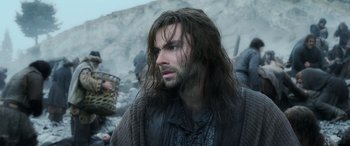 Movie still from “The Hobbit: The Battle of the Five Armies” (2014), directed by Peter Jackson – A man with long hair is standing in the dirt; Close Up shot, Over the shoulder angle