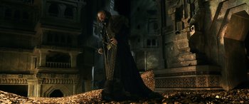 Movie still from “The Hobbit: The Battle of the Five Armies” (2014), directed by Peter Jackson – A man dressed in a long coat standing on a pile of coins; Wide shot, Low angle