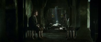 Movie still from “The Hobbit: The Battle of the Five Armies” (2014), directed by Peter Jackson – A man sitting on a chair in a dark room; Wide shot, High angle