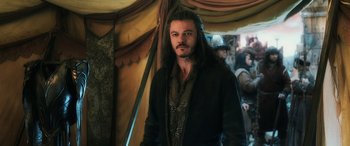 Movie still from “The Hobbit: The Battle of the Five Armies” (2014), directed by Peter Jackson – A man with long black hair standing in front of a tent; Medium shot, Over the shoulder angle