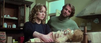 Movie still from “The House by the Cemetery” (1981), directed by Lucio Fulci – A man and a woman looking at a baby in a crib; Medium shot, Low angle