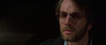 Movie still from “The House by the Cemetery” (1981), directed by Lucio Fulci – A person wearing a suit and glasses; Close Up shot, Over the shoulder angle