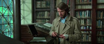Movie still from “The House by the Cemetery” (1981), directed by Lucio Fulci – A man in a library looking at his cell phone; Medium shot, Low angle