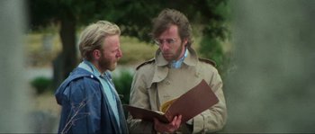 Movie still from “The House by the Cemetery” (1981), directed by Lucio Fulci – Two men are looking at a book together outside; Close Up shot, Over the shoulder angle