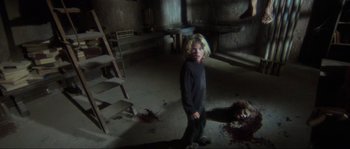 Movie still from “The House by the Cemetery” (1981), directed by Lucio Fulci – A little boy standing in a room with a dead body on the ground; Wide shot, High angle