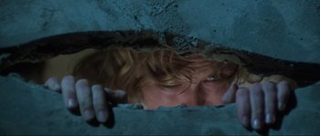 Movie still from “The House by the Cemetery” (1981), directed by Lucio Fulci – A man with long brown hair and green eyes looking out of a wall; Extreme Close Up shot, Low angle