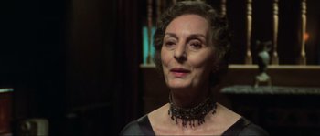 Movie still from “The House by the Cemetery” (1981), directed by Lucio Fulci – An older woman wearing a black dress and a black necklace; Close Up shot, Over the shoulder angle