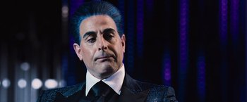 Movie still from “The Hunger Games” (2012), directed by Gary Ross – A man in a suit and tie with blue hair; Close Up shot, Over the shoulder angle