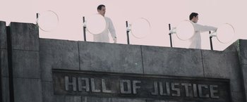 Movie still from “The Hunger Games” (2012), directed by Gary Ross – A man standing on top of a building with two frisbees in front of him; Extreme Wide shot, Low angle