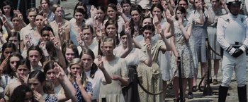 Movie still from “The Hunger Games” (2012), directed by Gary Ross – A large group of young people holding their hands up in the air; Medium shot, High angle