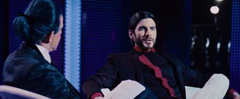 Movie still from “The Hunger Games” (2012), directed by Gary Ross – A man sitting on a couch in a room; Close Up shot, Over the shoulder angle