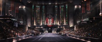 Movie still from “The Hunger Games” (2012), directed by Gary Ross – A large auditorium with stained - glass windows and an auditorium stage with people sitting in the seats; Extreme Wide shot, High angle