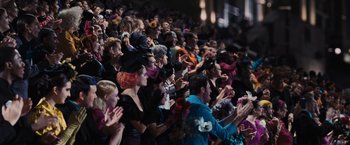 Movie still from “The Hunger Games” (2012), directed by Gary Ross – A group of people sitting in a crowd clapping; Wide shot, High angle