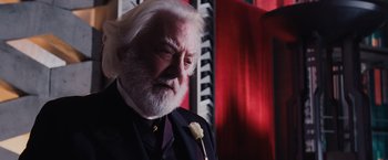 Movie still from “The Hunger Games” (2012), directed by Gary Ross – An older man with a white beard and a rose in his lapel; Close Up shot, Over the shoulder angle