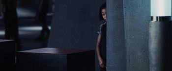 Movie still from “The Hunger Games” (2012), directed by Gary Ross – A young girl standing next to a wall in a dark room; Medium shot, Over the shoulder angle
