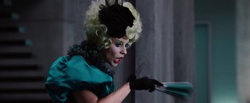 Movie still from “The Hunger Games” (2012), directed by Gary Ross – A woman with blonde curly hair wearing a blue dress and a black hat; Medium shot, Low angle