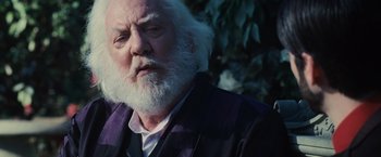 Movie still from “The Hunger Games” (2012), directed by Gary Ross – An old man with a beard and white hair; Close Up shot, Over the shoulder angle