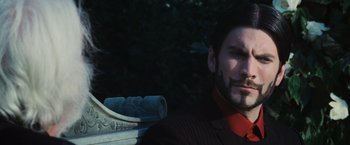 Movie still from “The Hunger Games” (2012), directed by Gary Ross – A man in a suit sitting in front of a statue; Close Up shot, Low angle