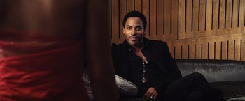 Movie still from “The Hunger Games” (2012), directed by Gary Ross – A man sitting in a chair in front of a wooden wall; Close Up shot, Over the shoulder angle