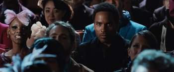 Movie still from “The Hunger Games” (2012), directed by Gary Ross – A man sitting in front of a crowd of onlookers; Close Up shot, Low angle