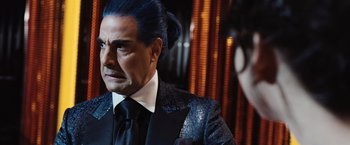 Movie still from “The Hunger Games” (2012), directed by Gary Ross – A man with blue hair wearing a suit and tie; Close Up shot, Over the shoulder angle