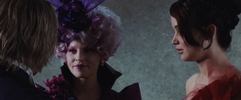 Movie still from “The Hunger Games” (2012), directed by Gary Ross – A woman in a purple wig and a purple hat; Close Up shot, Over the shoulder angle