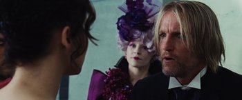 Movie still from “The Hunger Games” (2012), directed by Gary Ross – A man and a woman in a purple dress and a woman in a purple dress and a man in a purple suit; Close Up shot, Over the shoulder angle