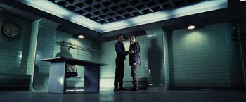 Movie still from “The Hunger Games” (2012), directed by Gary Ross – Two men standing in a room with a brick wall behind them; Wide shot, Low angle