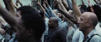 Movie still from “The Hunger Games” (2012), directed by Gary Ross – A group of people raising their hands in the air; Medium shot, Over the shoulder angle