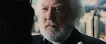 Movie still from “The Hunger Games” (2012), directed by Gary Ross – An older man with white hair and a white beard; Close Up shot, Over the shoulder angle