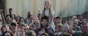 Movie still from “The Hunger Games” (2012), directed by Gary Ross – A girl sitting on the shoulders of a man in front of a crowd; Medium shot, Over the shoulder angle