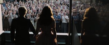 Movie still from “The Hunger Games” (2012), directed by Gary Ross – A woman in a red dress standing in front of an audience; Wide shot, Over the shoulder angle