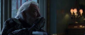Movie still from “The Hunger Games: Catching Fire” (2013), directed by Francis Lawrence – An older man with white hair wearing gloves; Close Up shot, Over the shoulder angle