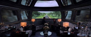 Movie still from “The Hunger Games: Catching Fire” (2013), directed by Francis Lawrence – Two men sitting on a couch in front of a large window; Wide shot, High angle