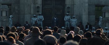 Movie still from “The Hunger Games: Catching Fire” (2013), directed by Francis Lawrence – A crowd of people standing in front of a building; Wide shot, Over the shoulder angle